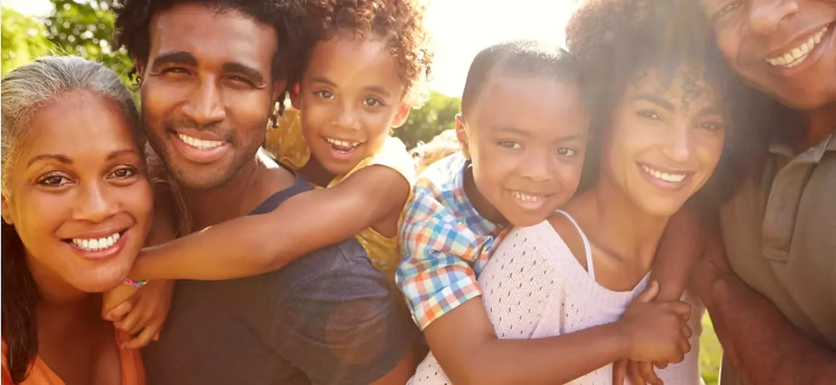 Three generations of a smiling Black family gathered close together outdoors